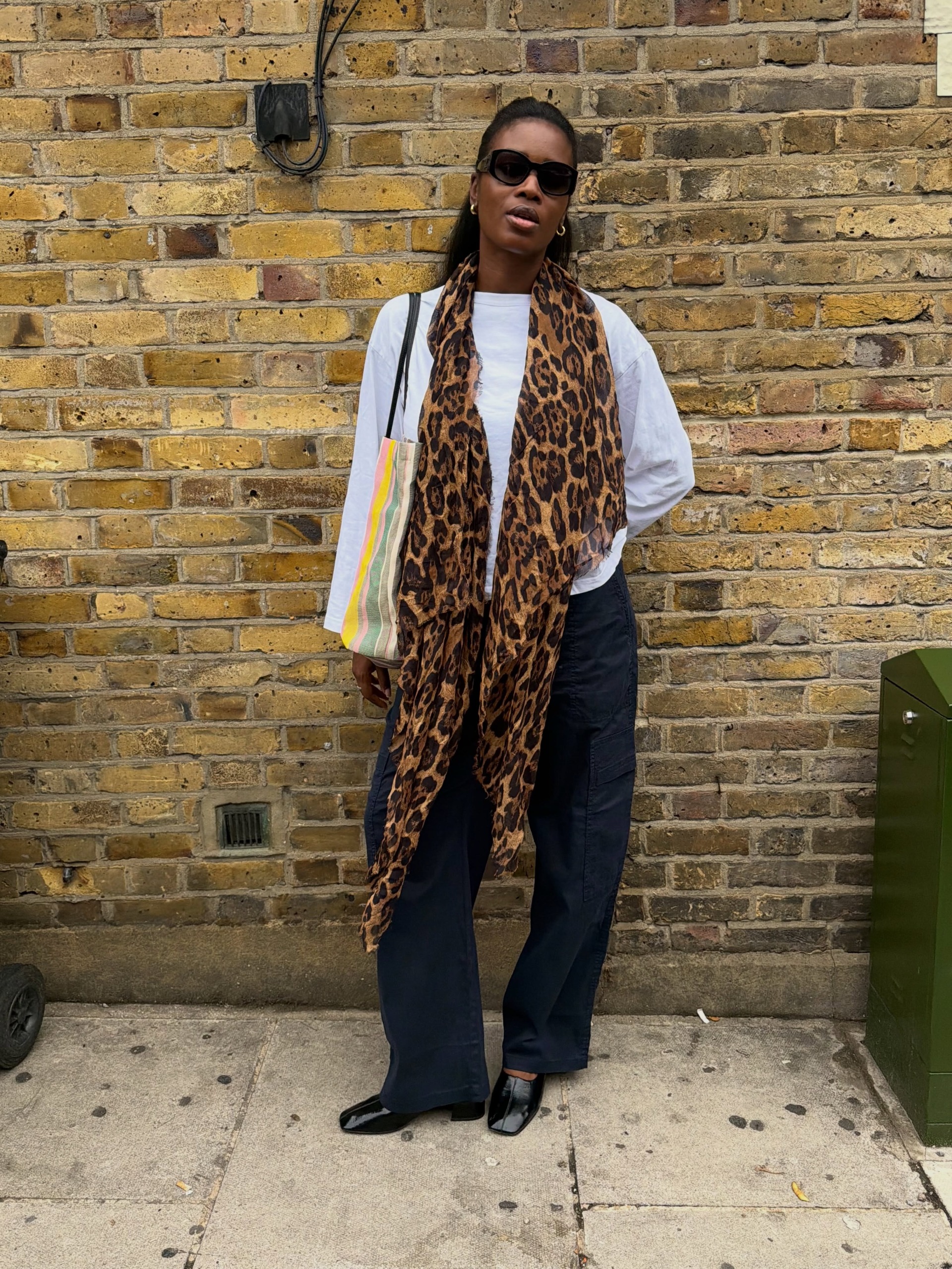 fashion influencer wearing a long-sleeve white tee, leopard-print scarf, black pants, and high-vamp pumps