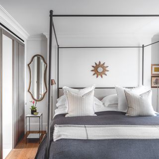 White bedroom with a modern black framed bed with a shapely wall mirror next to the alcove