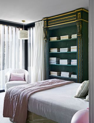 Small bedroom with pink bedlinen and green painted bookcase