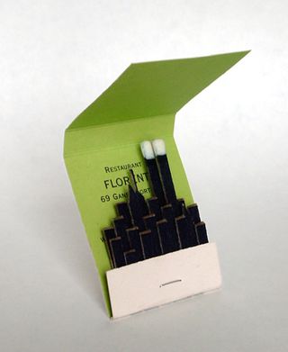 green match book with black matches in the shape of the New York Skyline