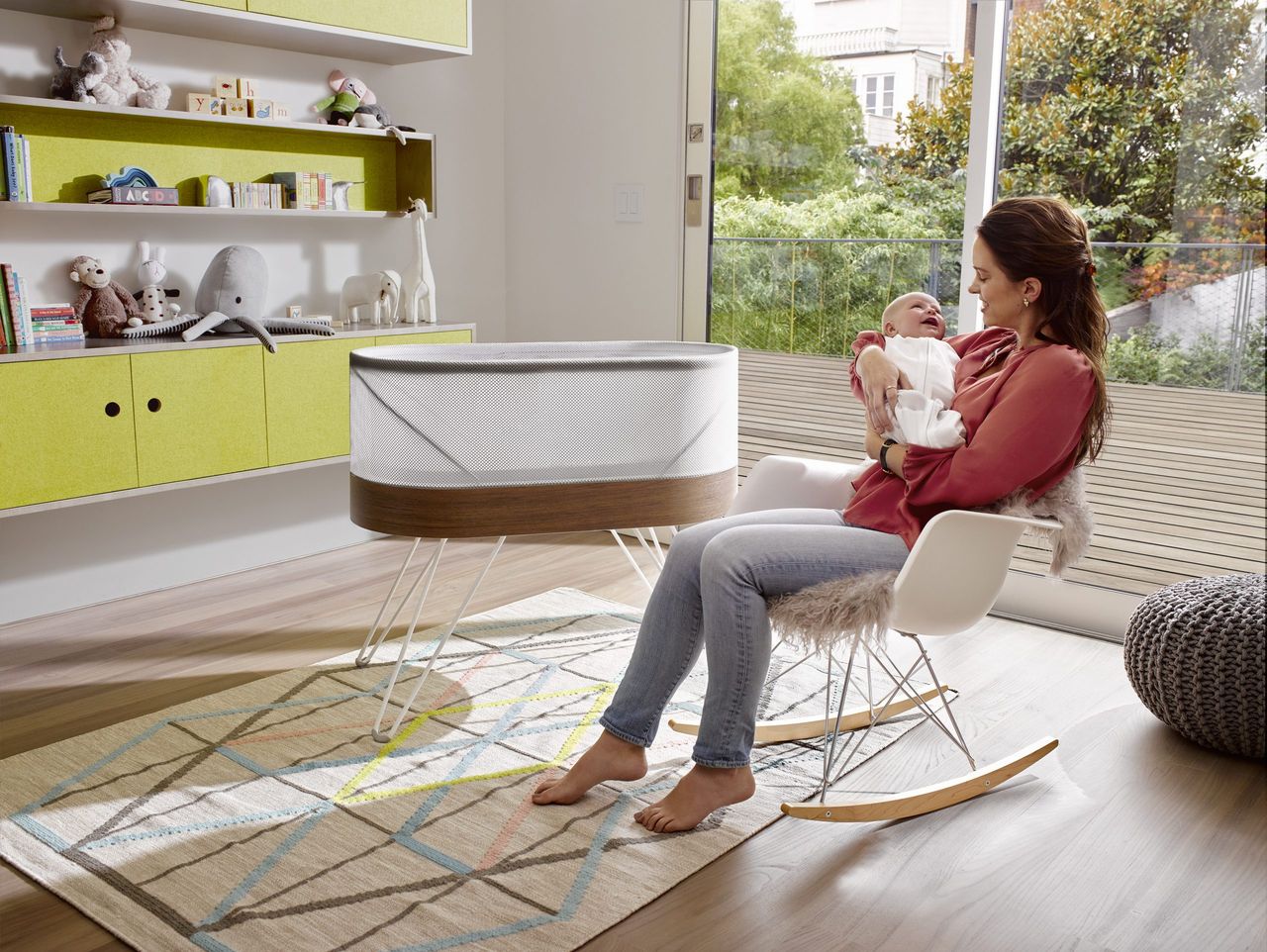 A woman cradles a sleeping newborn beside the Snoo Smart Sleeper Baby Cot