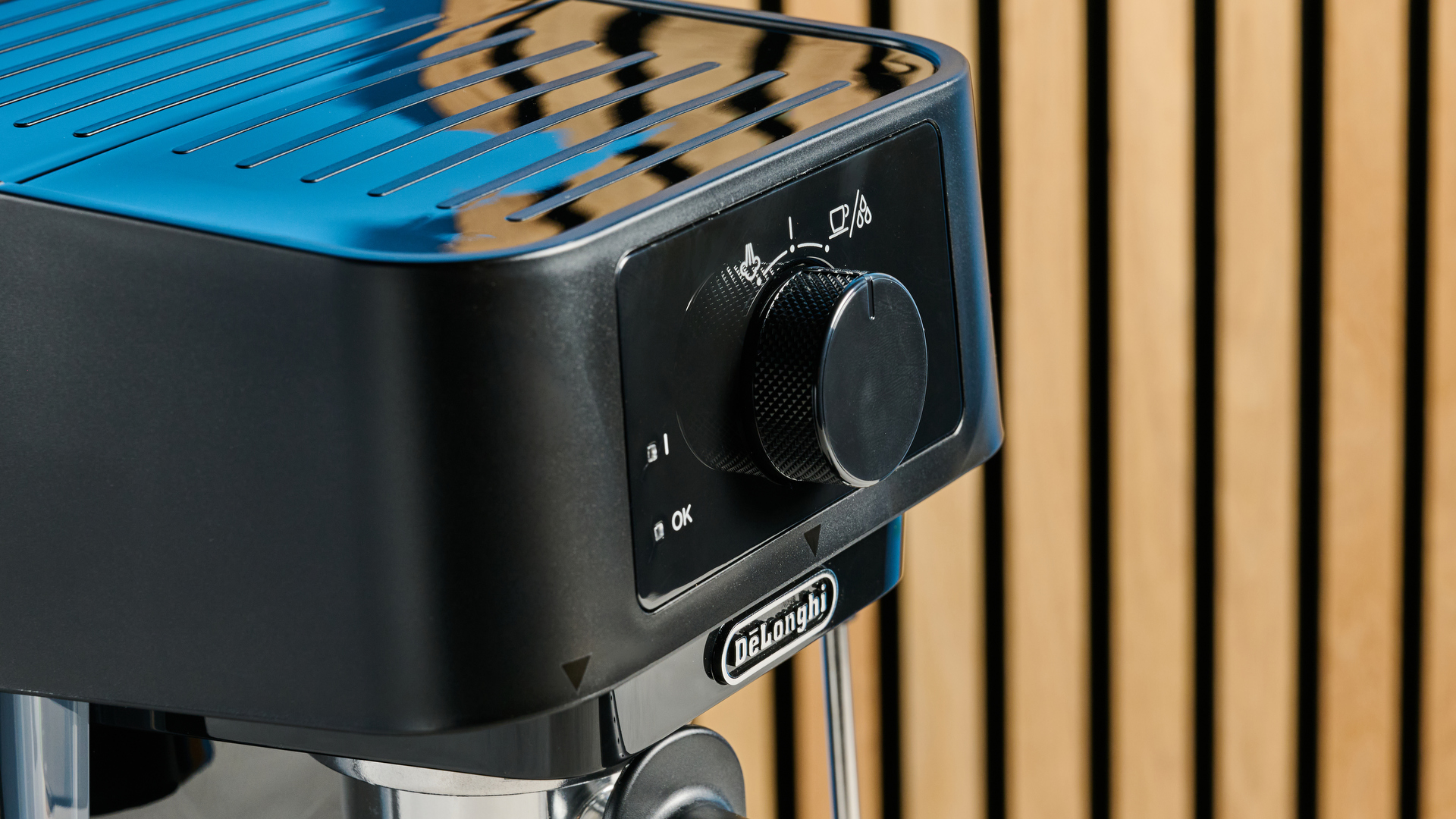 the de'longhi stilosa espresso machine in black, with one portafilter, a dial for espresso and milk steaming, and a plastic tamper, photographed against a blue background
