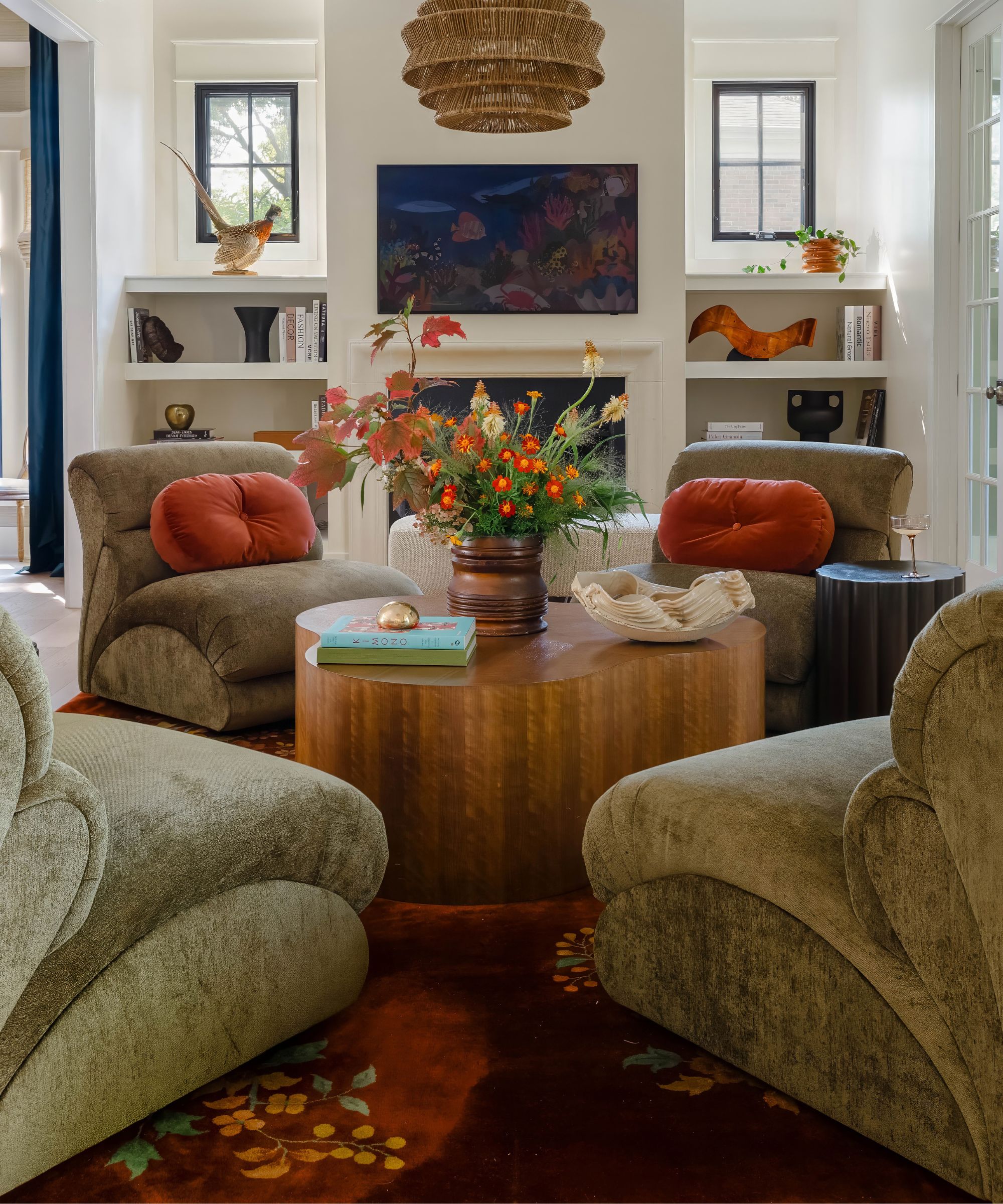 neutral living room with a fireplace, niche shelves, and a round wooden coffee table styled with 4 green velvet arm chairs around it