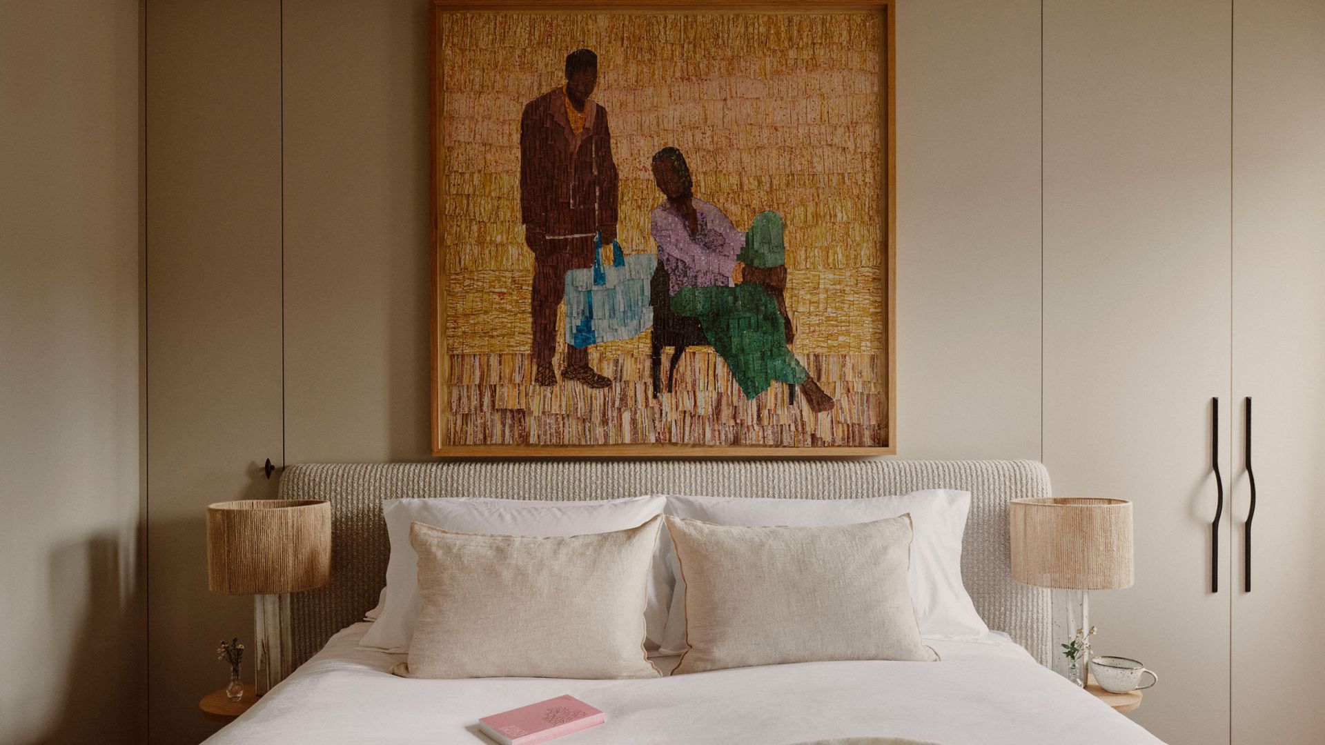 A simple bedroom with a large bed and a textured headboard, a set of textured lamps on either side table, a framed painting above, and a small closet to the right