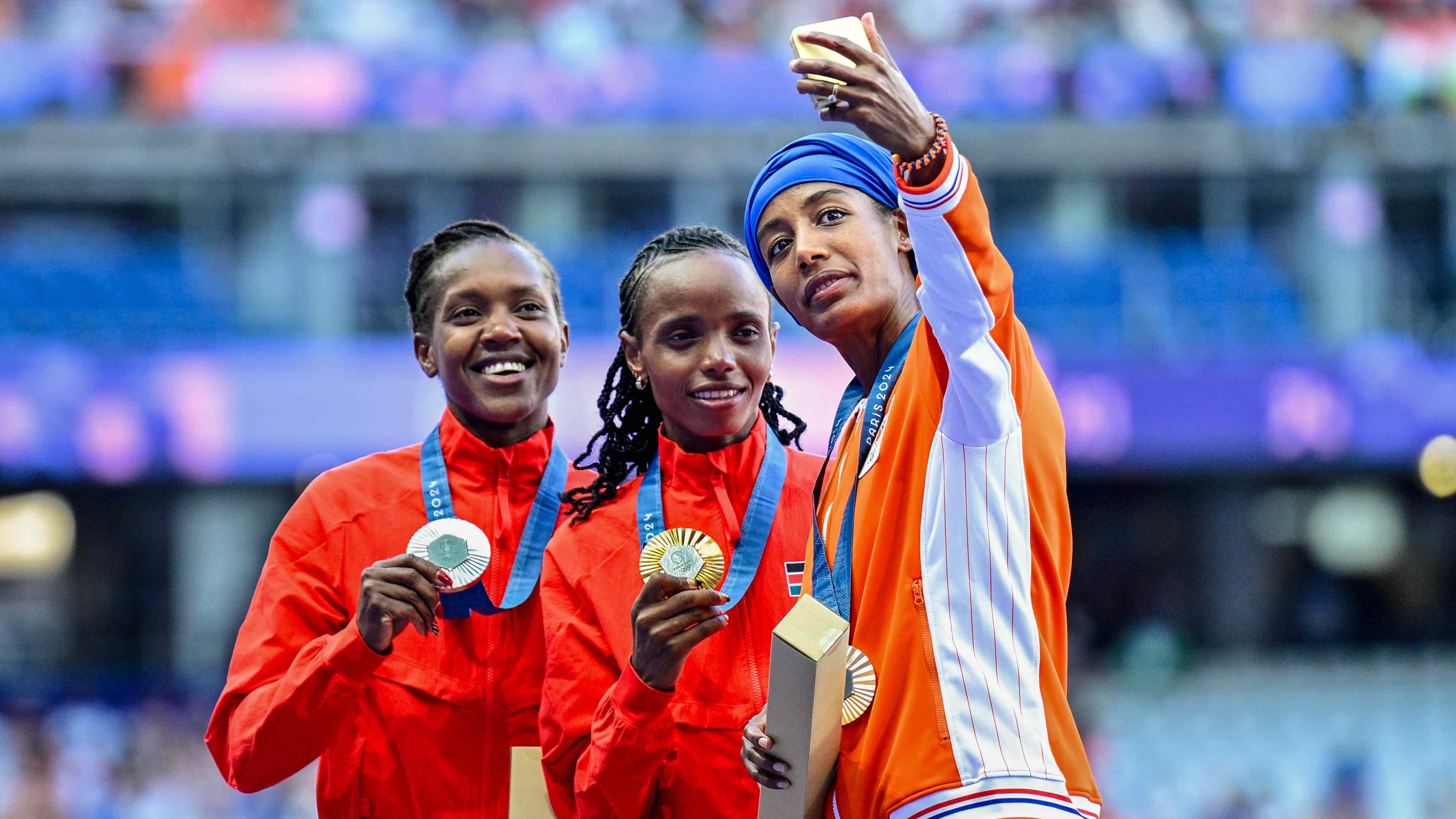 Beatrice Chebet of Kenya winner of the silver medal, Faith Kipyegon of Kenya winner of the gold medal, and Team Samsung Galaxy’s Sifan Hassan of the Netherlands, winner of the bronze medal, take a victory selfie with the Samsung Galaxy Z Flip6 Olympic Edition during the medal ceremony after competing in the Women's 5000m Final - Medal Ceremony during Day 11 of Athletics - Olympic Games Paris 2024 at Stade de France on August 6, 2024 in France. (Photo by Andy Astfalck/BSR Agency/Getty Images)