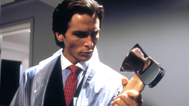 A still from the movie American Psycho in which Patrick Bateman (Christian Bale) is wearing a suit and looking at an axe.