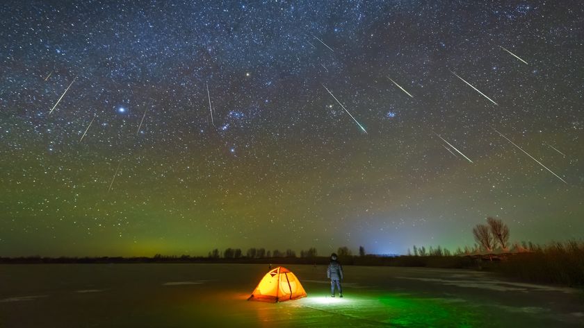 a camper stands outside a tent as the night sky is lit up by a meteor shower