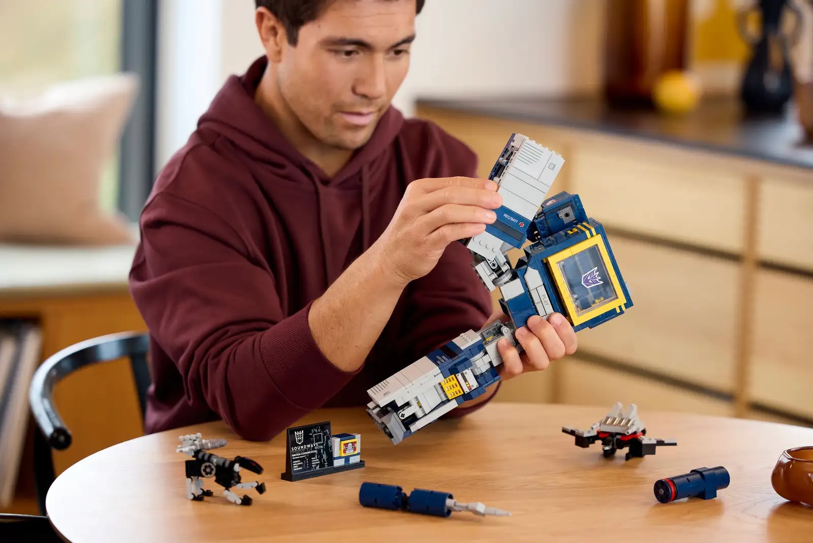 LEGO Transformers Soundwave being built by a man in a hoodie at a table 