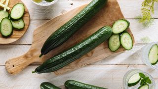 A cucumber on a chopping board, surrounded by slices