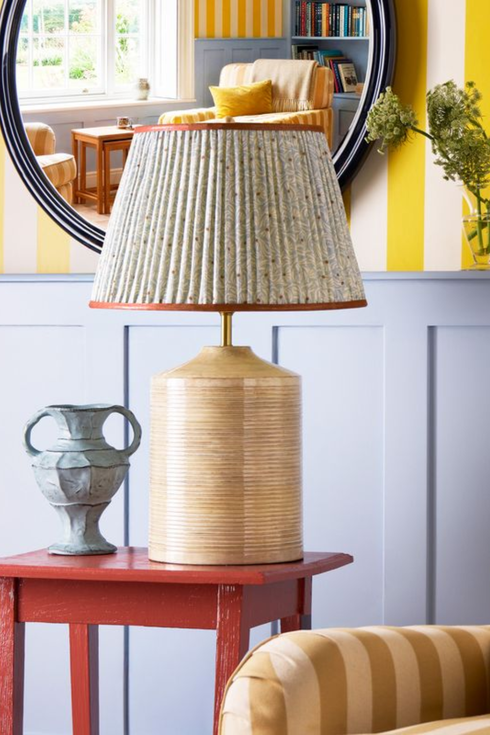 Floral patterned Pooky table lamp styled atop of a red side table in a colorful sitting room