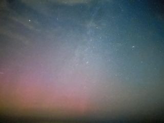 a star filled sky with a hazy red aurora present in the lower left portion of the image.