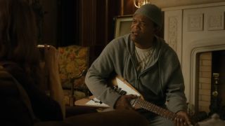 Samuel L Jackson playing a guitar while talking in front of a fireplace in The Protégé.
