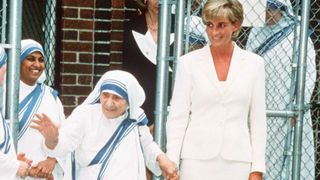 Mother Teresa in her tradition white and blue attire holding hands with Princess Diana in a white skirt suit