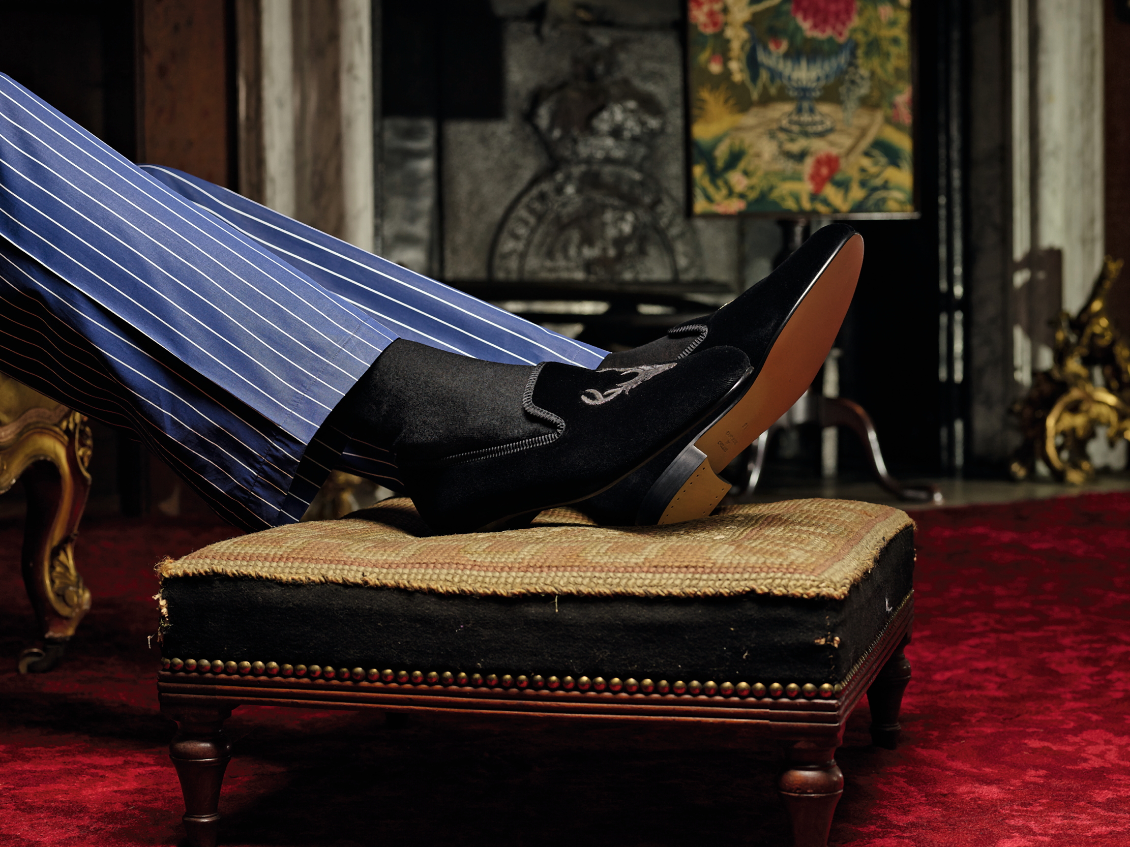 A man wearing a pair of slippers, resting his trotters on a little footstool