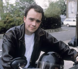 Mark Fowler on a motorbike and wearing a leather jacket.