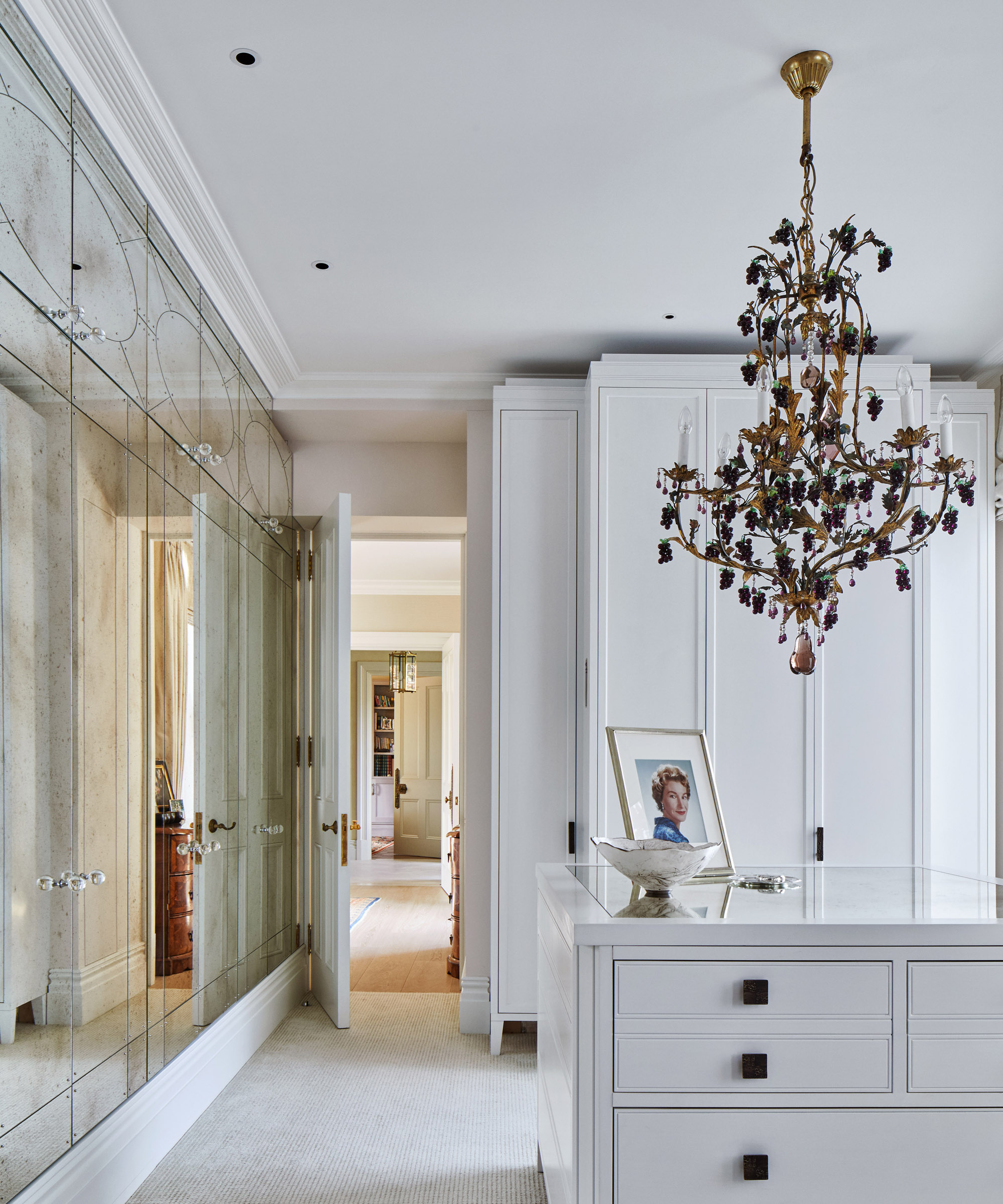 An example of bedroom chandelier ideas showing a white dressing room with a mirrored wall and gold and black chandelier