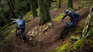 Two riders negotiate a tight right hand switch back on a trail snacking through trees