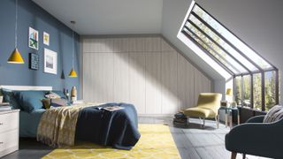 loft bedroom with large window, built in wardrobes, double bed, armchairs, decorated in blue, yellow and pale grey colour scheme