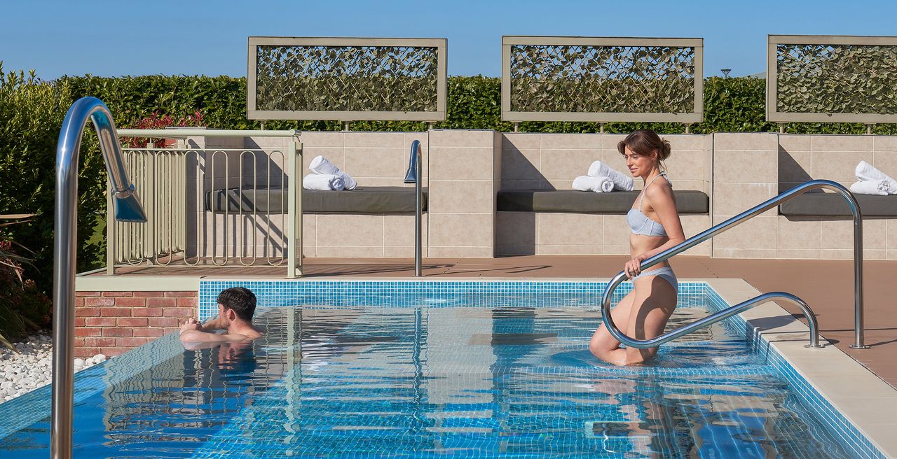 A woman walking into a swimming pool with a man resting his arms over the edge looking at the view