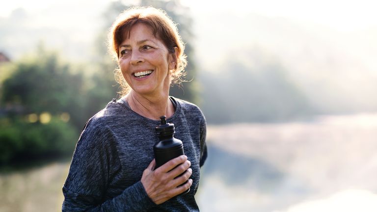 A woman looks happy as she exercises outdoors holding a water bottle