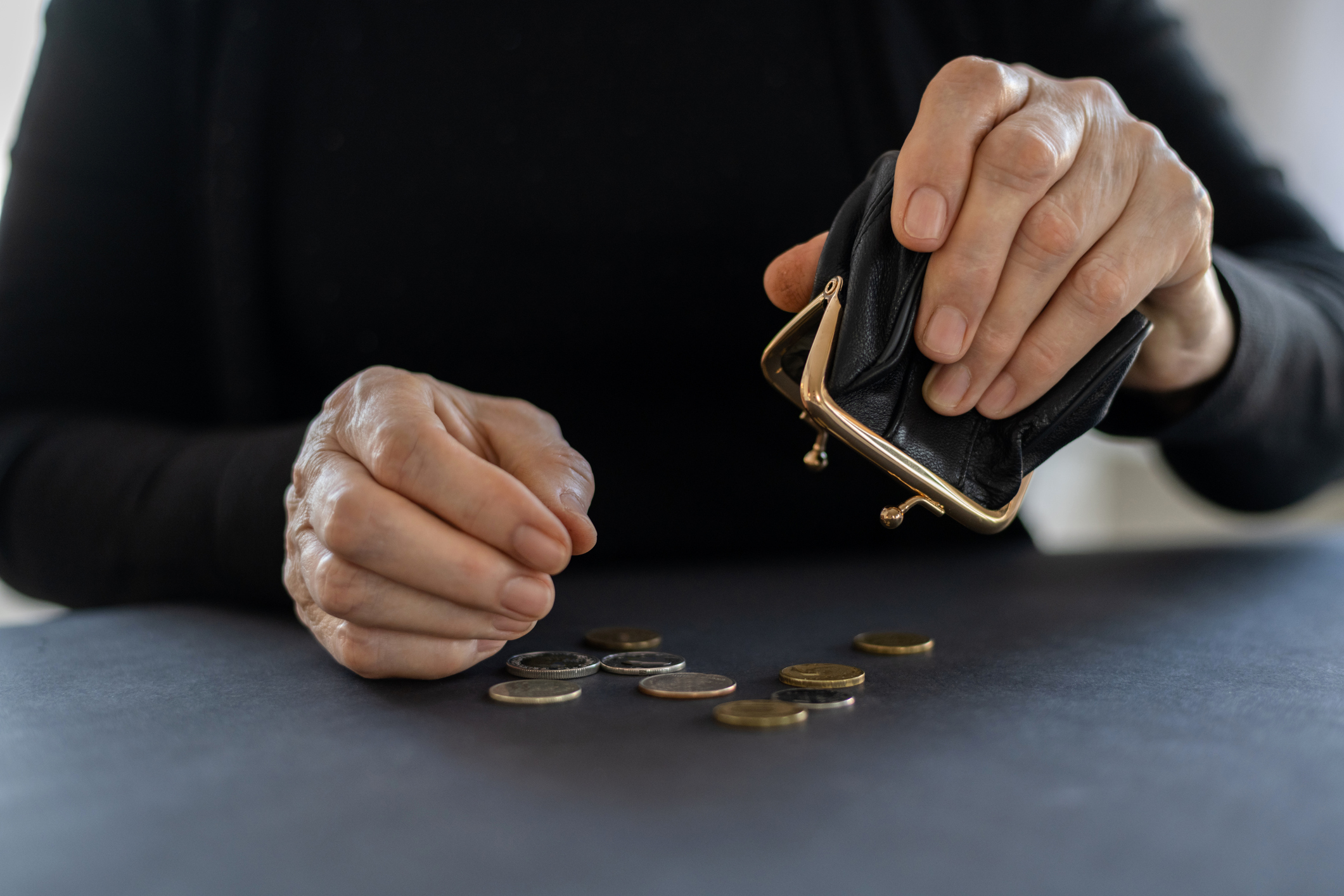 An elderly woman holds an open black empty coin purse in her hands on the lap, the concept of poverty, finance, retirement