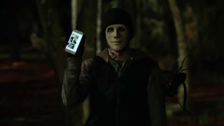 The masked killer from Mike Flanagan&#039;s Hush showing off a phone.