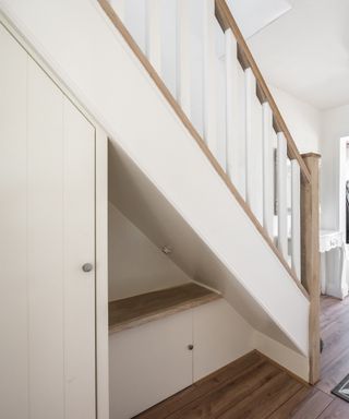 An image of a white stair case with wooden hand rails and an under stair storage box