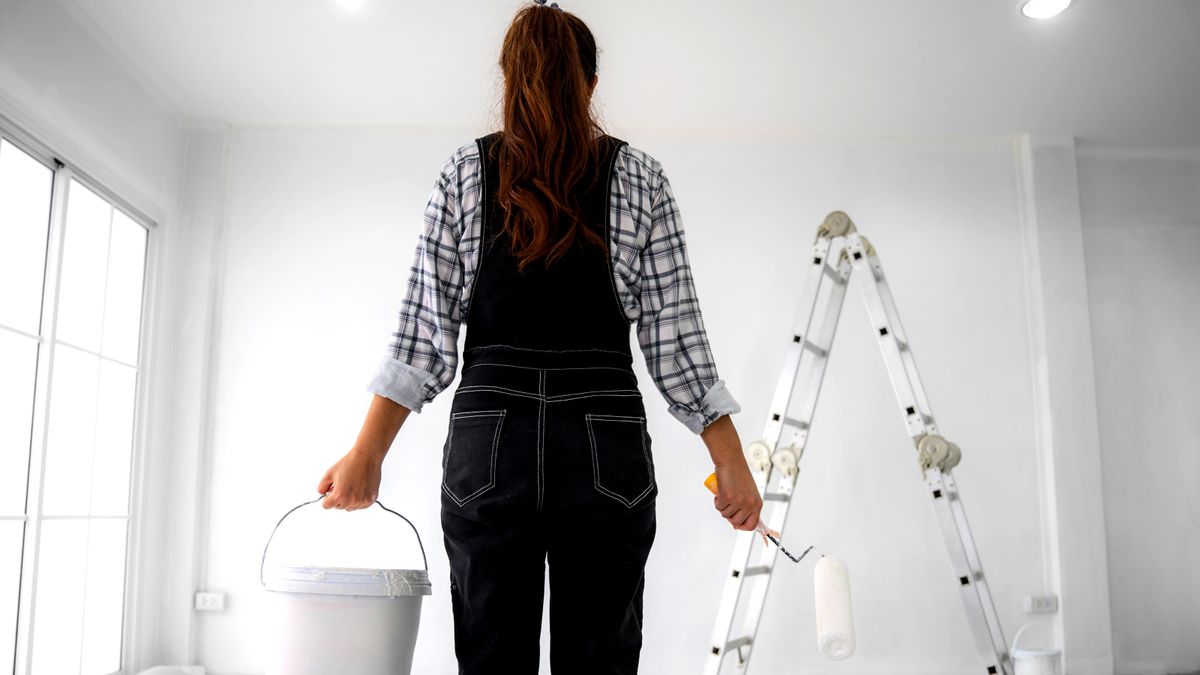 Woman standing in front of white wall with bucket and roller in hand