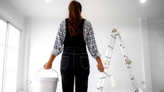 Woman standing in front of white wall with bucket and roller in hand