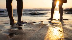 Low shot of two people silhouetted on a sandy beach at sunset