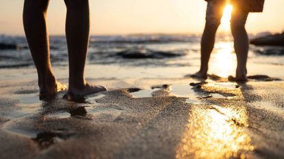 Low shot of two people silhouetted on a sandy beach at sunset