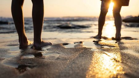 Low shot of two people silhouetted on a sandy beach at sunset