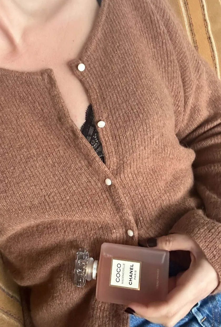 Shannon wearing a brown cardigan and holding a bottle of Chanel Mademoiselle