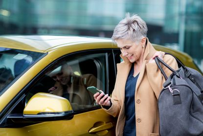 A woman with a duffel bag checks her phone before getting into her rental car.