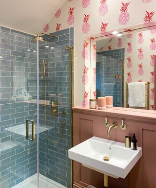 A shower room with blue tiles, pink pineapple wallpaper, and a white sink on a pink wall