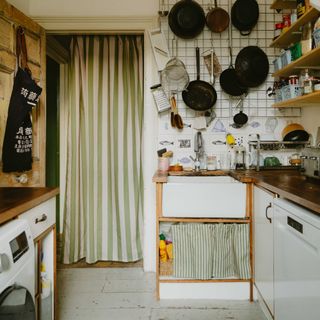 A small kitchen with hanging pans and striped curtains