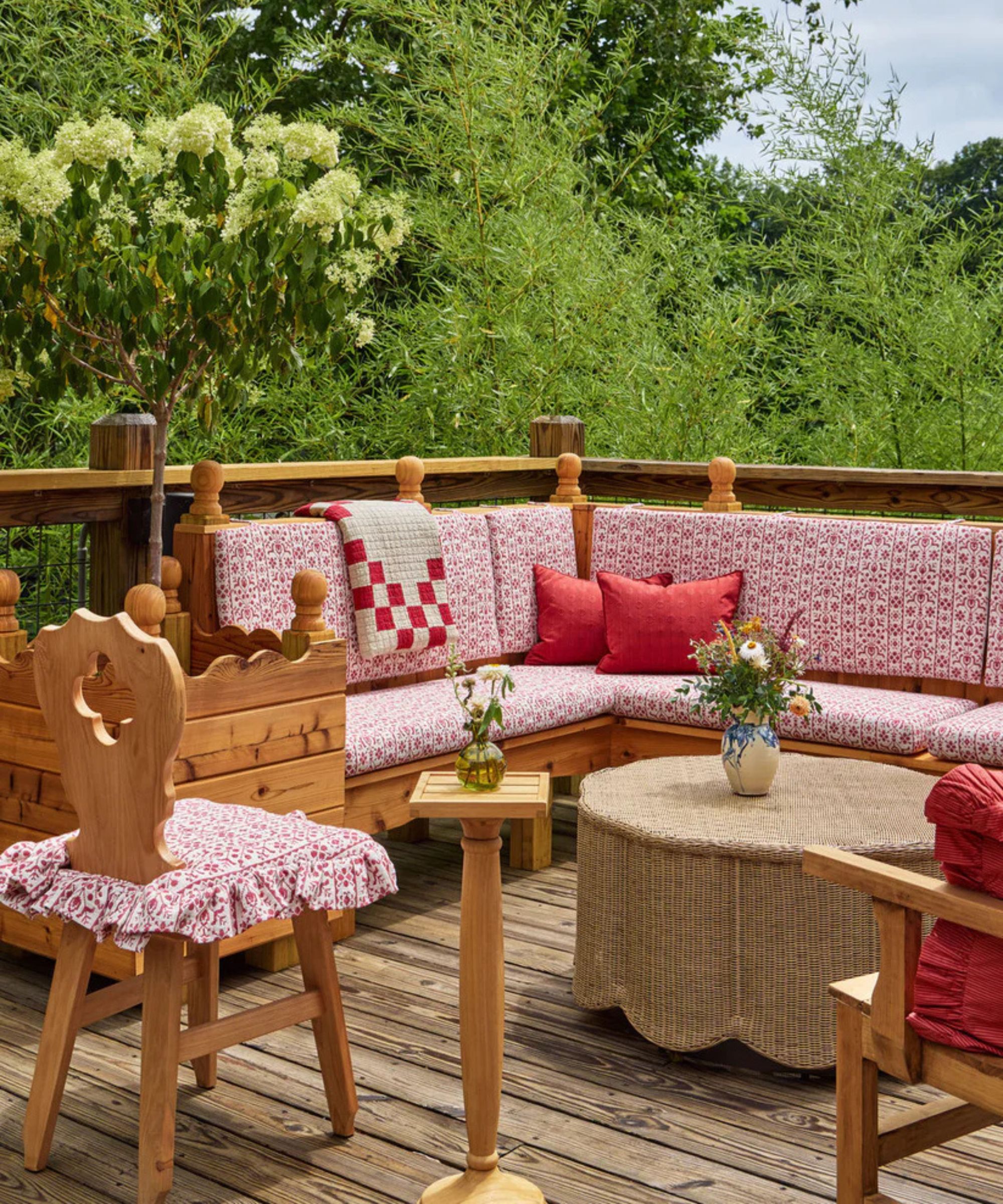 large wooden balcony patio with pine corner sofa styled with red and white patterned cushions, a patchwork throw and red cushions with a rattan scalloped coffee table and vintage pine dining chair