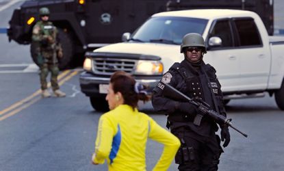 A runner passes a police officer and team blocking a road leading to the Boston Marathon rout the morning after the explosions.