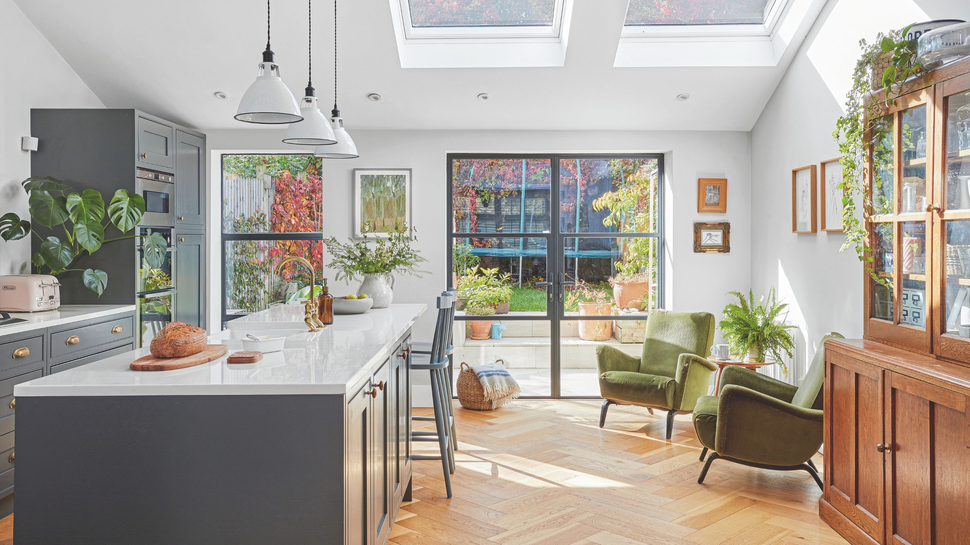 Large open plan kitchen and seating area with blue cabinets and a matching kitchen island, with two green accent chairs on the right next to a wooden storage unit