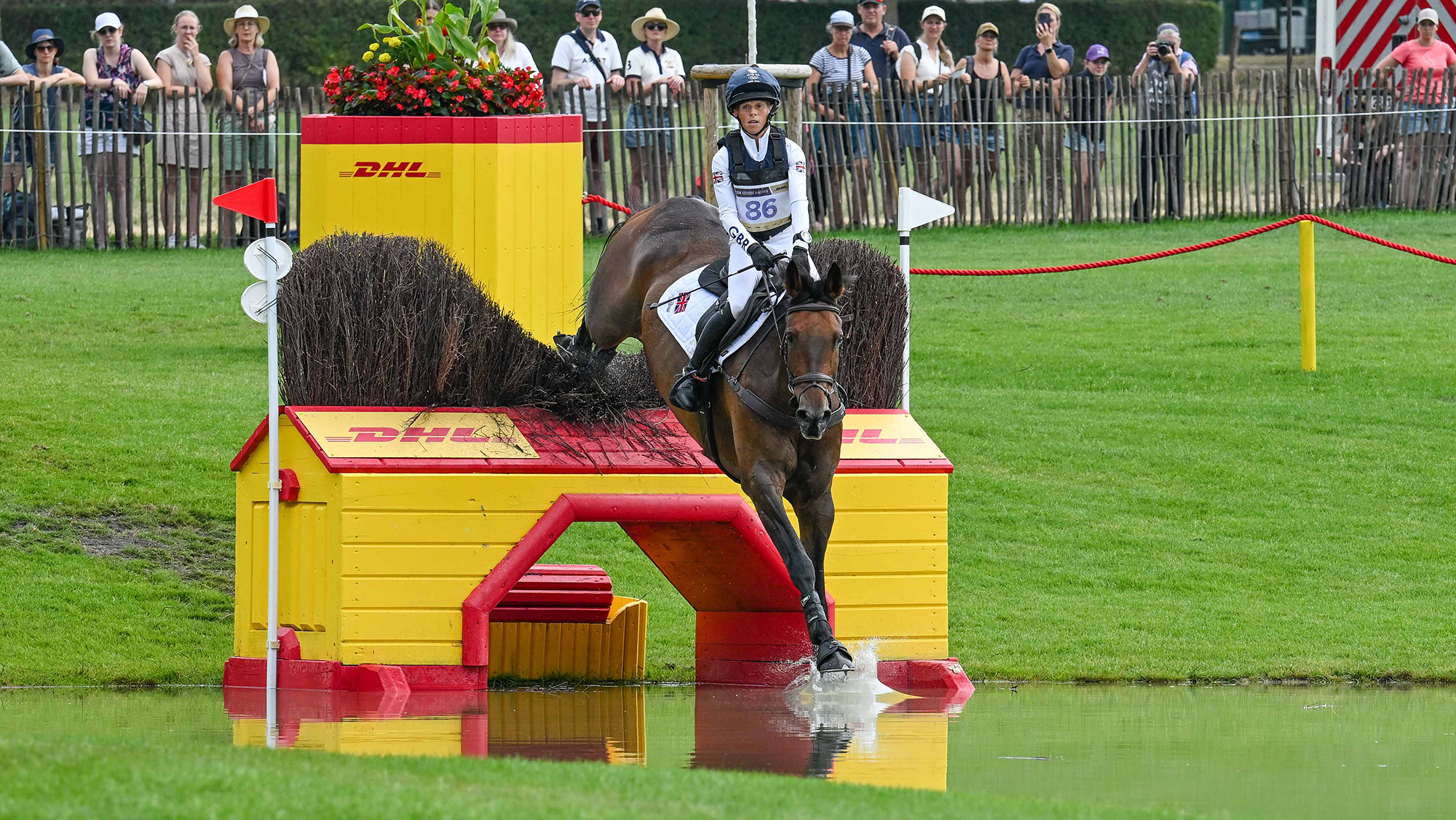 Ros Canter and Lordships Graffalo jump a bright red and yellow DHL-branded cross country jump into water at Aachen 2026 World Eventing Championships