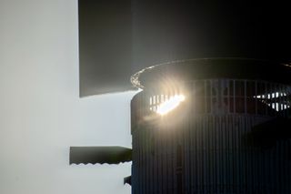 part of the sun shines through the vented interstage ring at the top of SpaceX's Superheavy booster. A grid fin is seen extended.