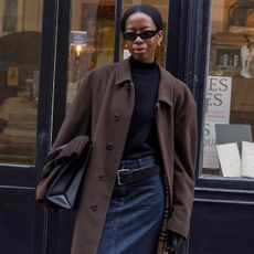 French influencer wearing black turleneck sweater, denim midi skirt, brown coats, tights, and black heeled mules.