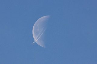 A passenger plane cruises at 40,000 feet (12,000 meters), passing in front of the half moon.