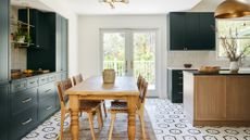 A kitchen with a hexagonal mosaic floor, green cabinetry and rustic wooden dining table
