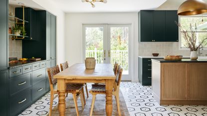 A kitchen with a hexagonal mosaic floor, green cabinetry and rustic wooden dining table