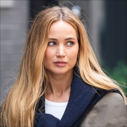 Jennifer Lawrence has long blonde hair and wears a navy sweater tied around her shoulders in SoHo on June 28, 2023 in New York City
