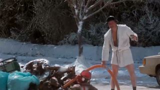 Randy Quaid in a bathrobe holding a tube