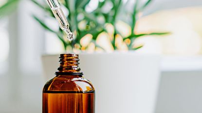 Close up of face serum pouring from a pipette into an amber glass bottle.