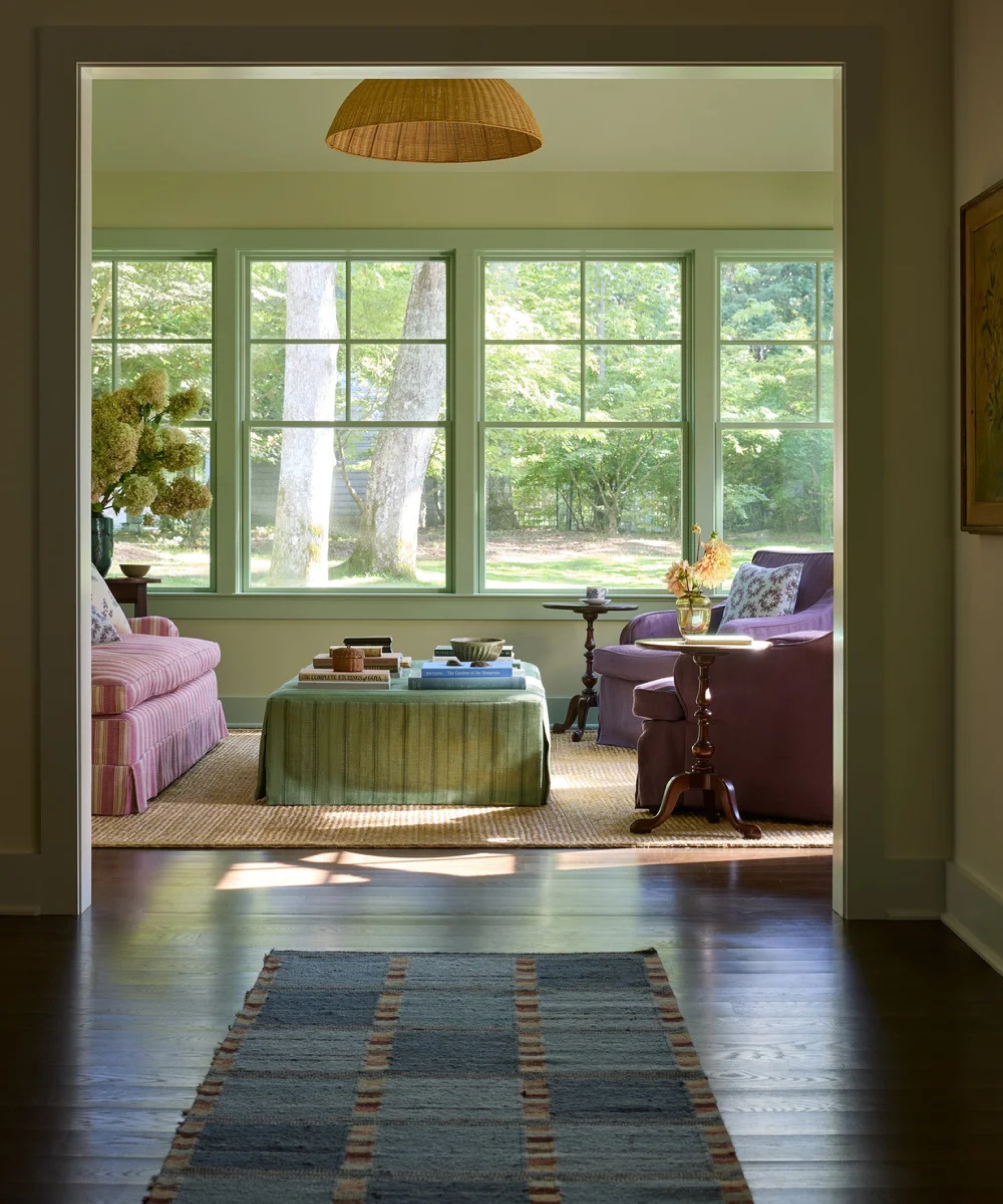 Sun filled pale yellow sunroom with pale green windows and a pink sofa with purple armchairs