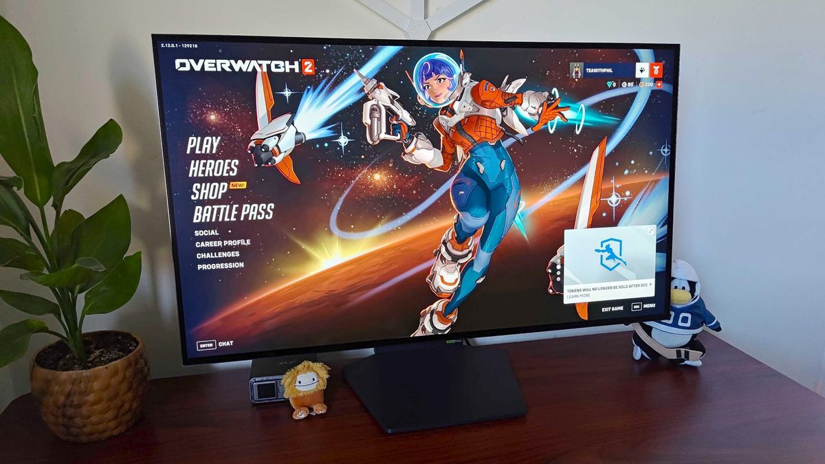 LG UltraGear 32GS95UE-B on woodgrain desk with Overwatch 2 main menu on screen